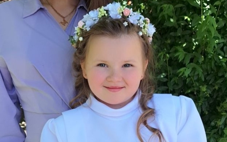 Uśmiechnięta dziewczynka w białej sukience z kwiatami we włosach.