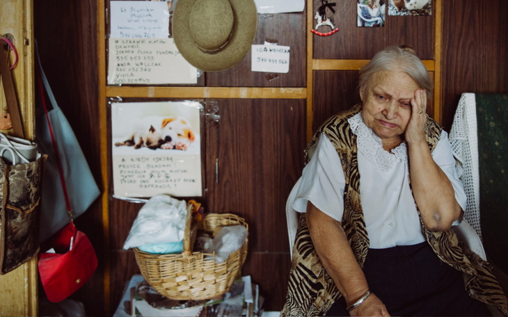 Starsza kobieta siedzi w pomieszczeniu, wygląda na zamyśloną.