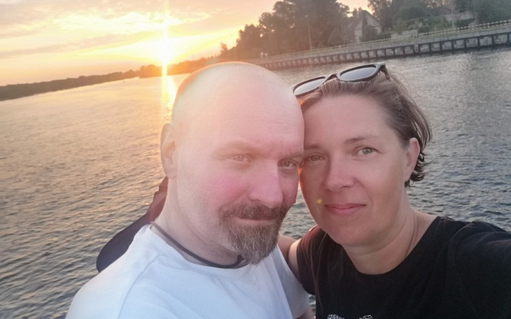 Para na tle zachodzącego słońca, uśmiechająca się do zdjęcia.