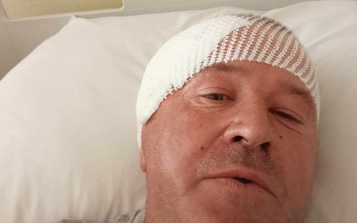 Mężczyzna z opatrunkiem na głowie, w szpitalnym łóżku.