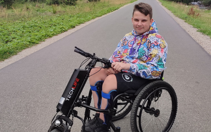 Chłopiec na wózku inwalidzkim, uśmiechnięty na drodze.