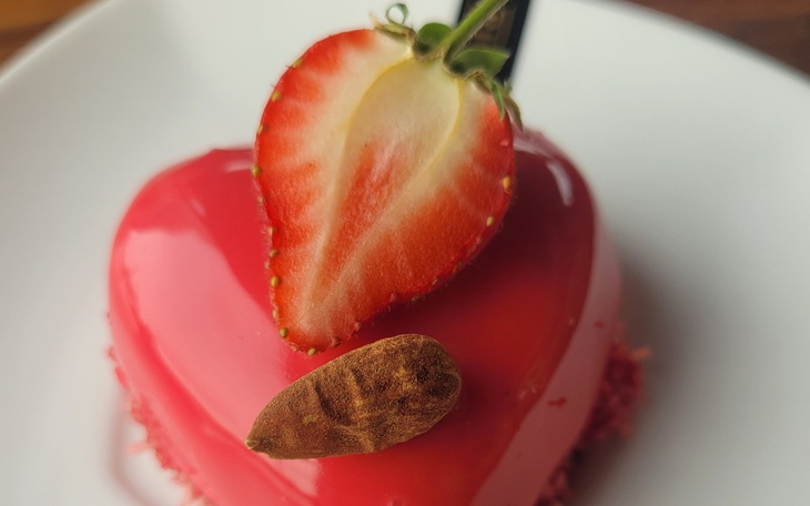 Czerwony tort w kształcie serca z truskawką na wierzchu.