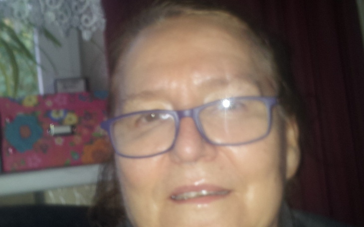 Kobieta w okularach, uśmiechająca się do kamery, w tle kolorowe tło.