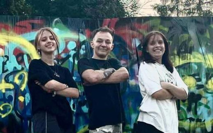 Trójka młodych ludzi pozująca przed kolorowym muralem.