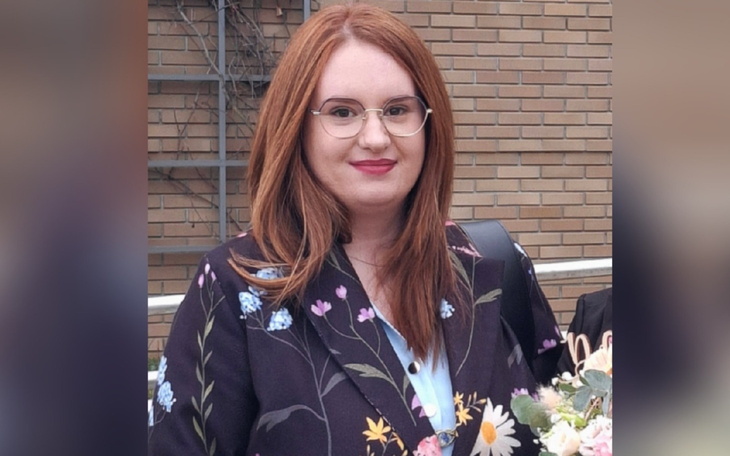 Kobieta z rudymi włosami, uśmiechająca się na tle budynku.