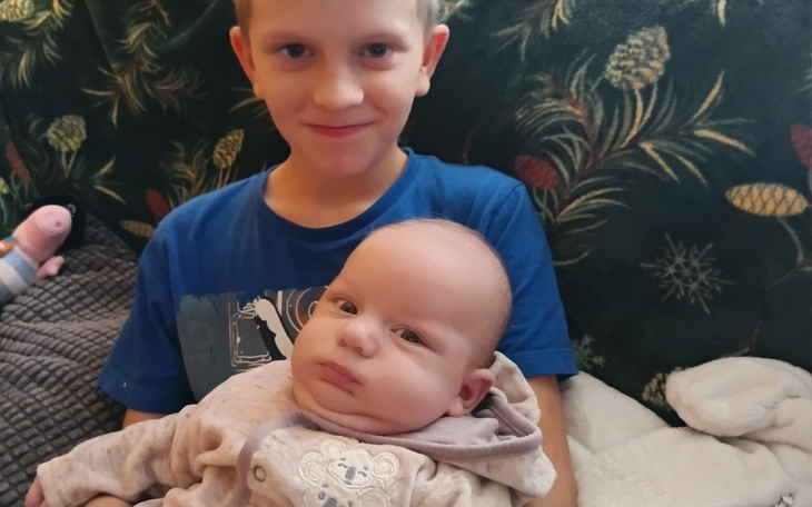 Chłopiec trzymający niemowlę na kolanach, oboje uśmiechnięci.