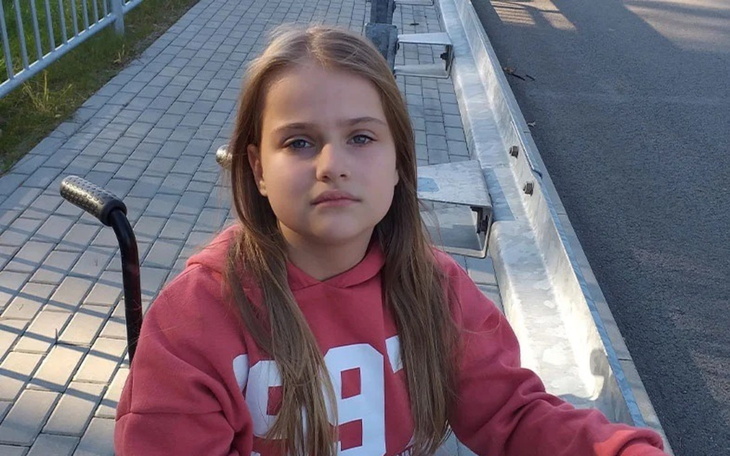 Dziewczynka w wózku, patrzy w obiektyw, na tle chodnika.