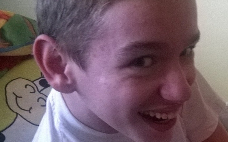 Chłopak z uśmiechem na twarzy, siedzący na łóżku.