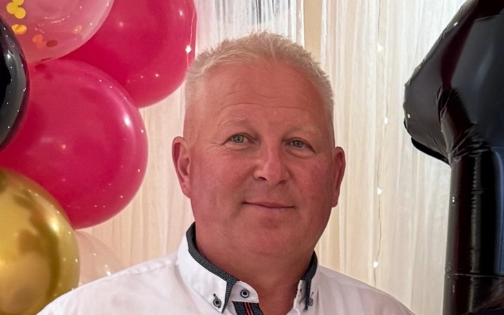 Mężczyzna uśmiechający się na tle kolorowych balonów.