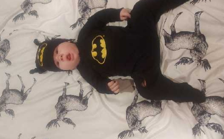 Mały chłopiec w czarnym kostiumie Batmana, leżący na pościeli.