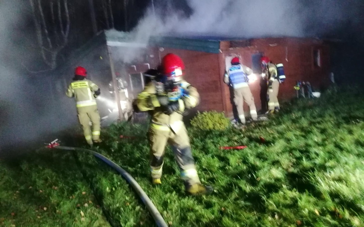 Strażacy gaszą pożar w drewnianym budynku.