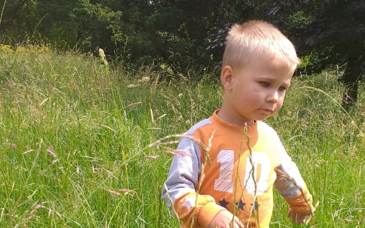 Mały chłopiec spacerujący po łące, otoczony trawą.