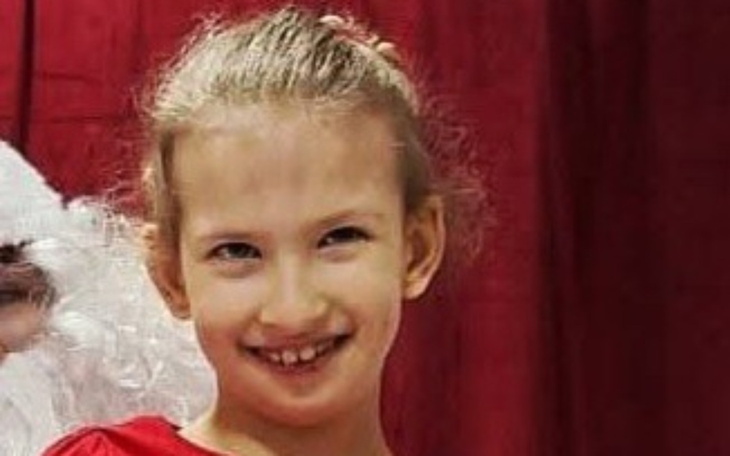 Uśmiechnięta dziewczynka w czerwonej sukience, pozująca na tle.