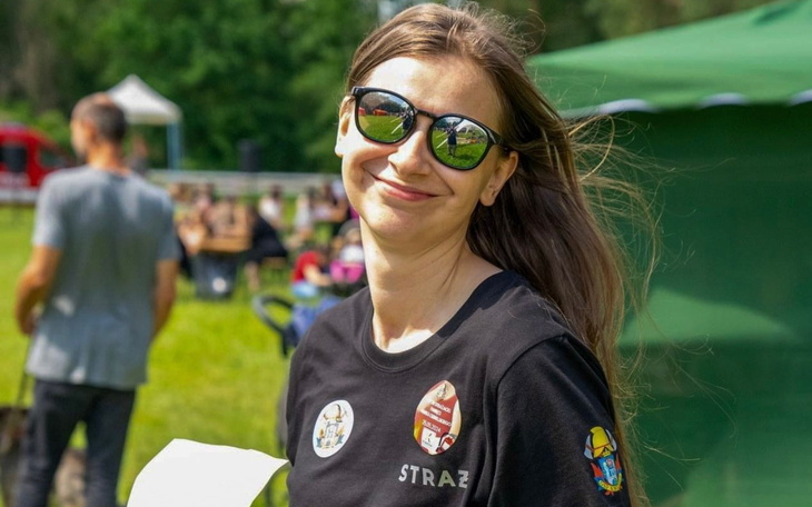 Uśmiechnięta kobieta w okularach przeciwsłonecznych na tle zieleni.