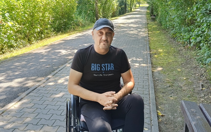 Mężczyzna na wózku inwalidzkim odpoczywający na ścieżce w parku.