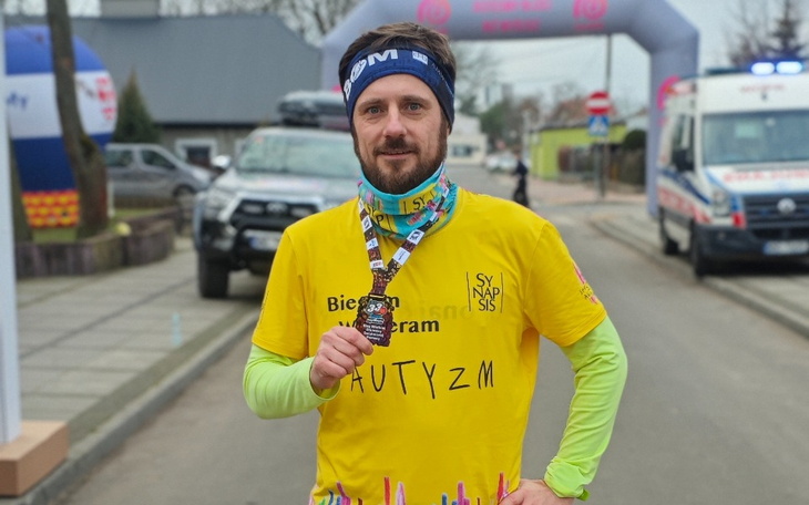 Mężczyzna po biegu, trzyma medal i uśmiecha się.