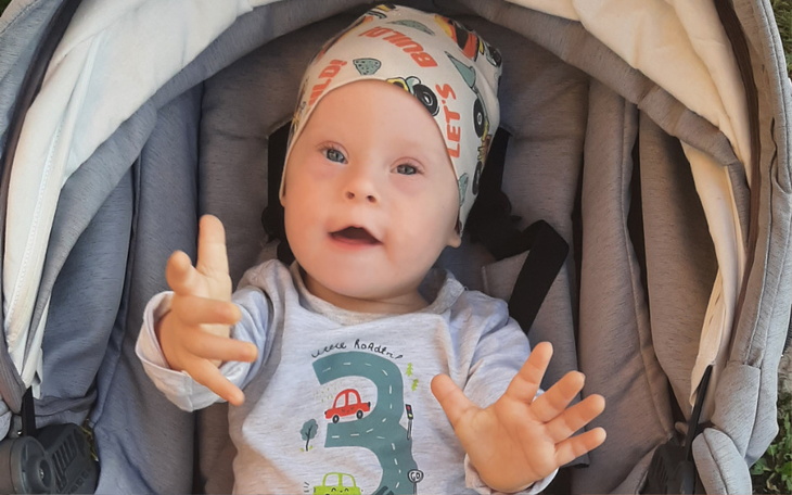 Małe dziecko w wózku, uśmiechające się i wyciągające rączki.