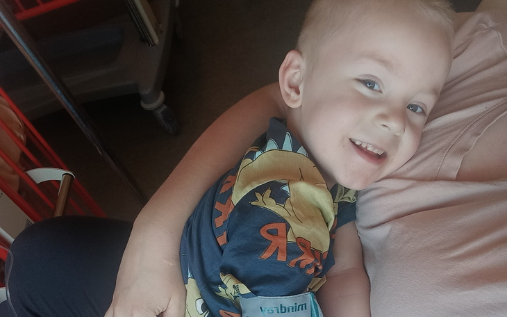 Mały chłopiec uśmiechający się, trzymany na rękach przez dorosłego.