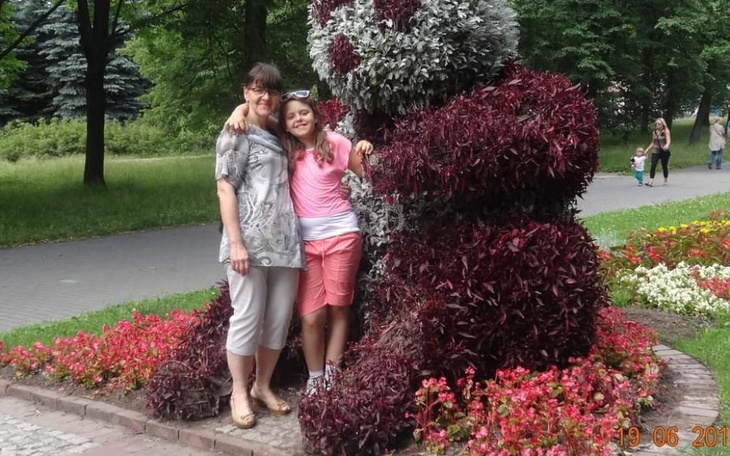 Dzieci z dorosłymi przy rzeźbie z roślin w parku.