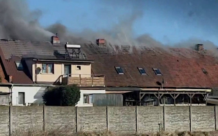 Dach domu w ogniu, dym unoszący się w powietrzu.