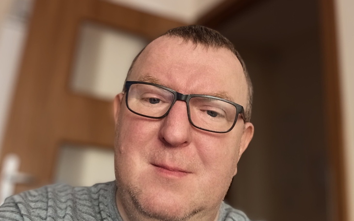 Mężczyzna w okularach, uśmiechający się do kamery.