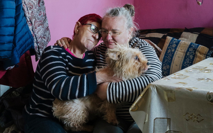 Dwie kobiety przytulają się z psem w przytulnym wnętrzu.