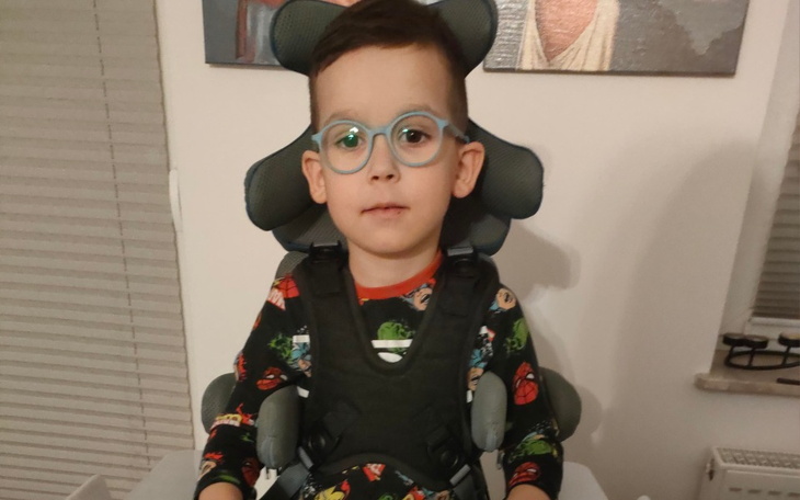 Chłopiec w foteliku, noszący okulary i uśmiech.