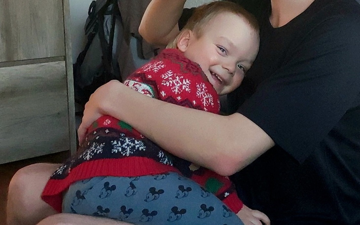 Dziecko w swetrze, uśmiechające się w ramionach opiekuna.