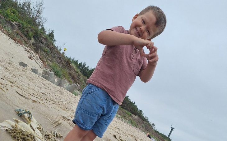 Chłopiec na plaży, robiący serce z rąk.