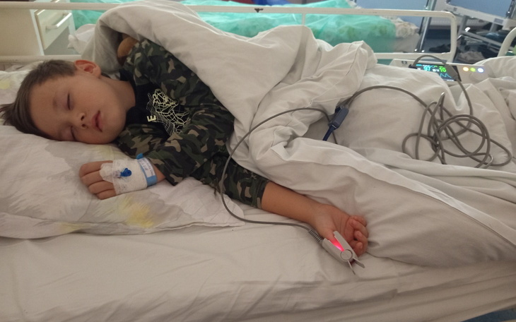 Chłopiec śpiący w szpitalnym łóżku z kroplówką.