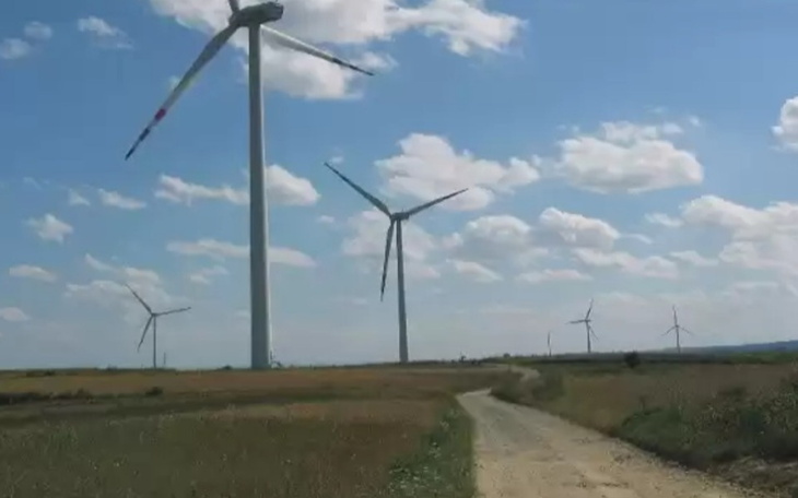 Widok na wiatraki na tle błękitnego nieba i zielonych pól.
