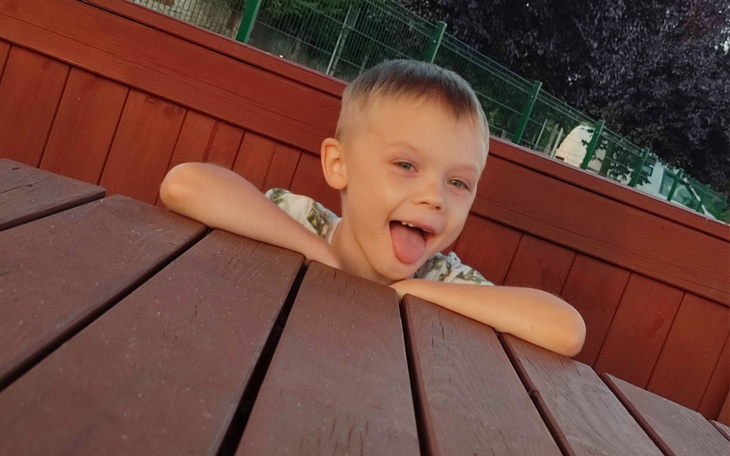 Chłopiec z uśmiechem i wystawionym językiem przy stole.