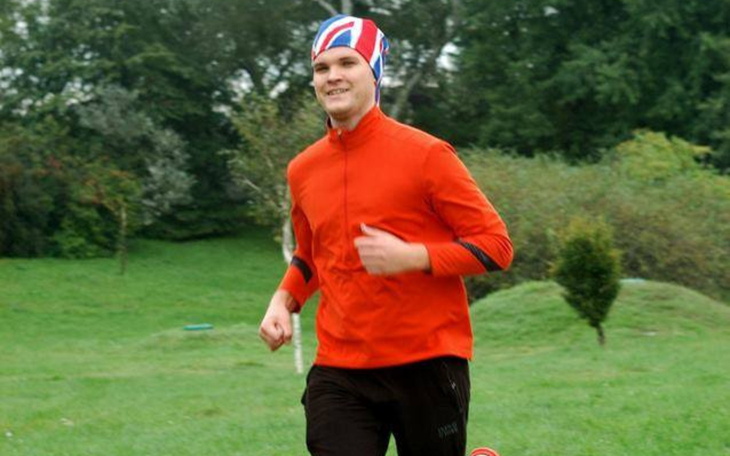 Mężczyzna biegający w parku, ubrany w czerwoną bluzę i czapkę.