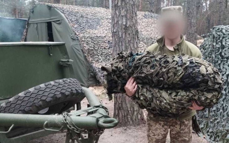 Żołnierz trzymający zamaskowanego psa w obozie wojskowym.