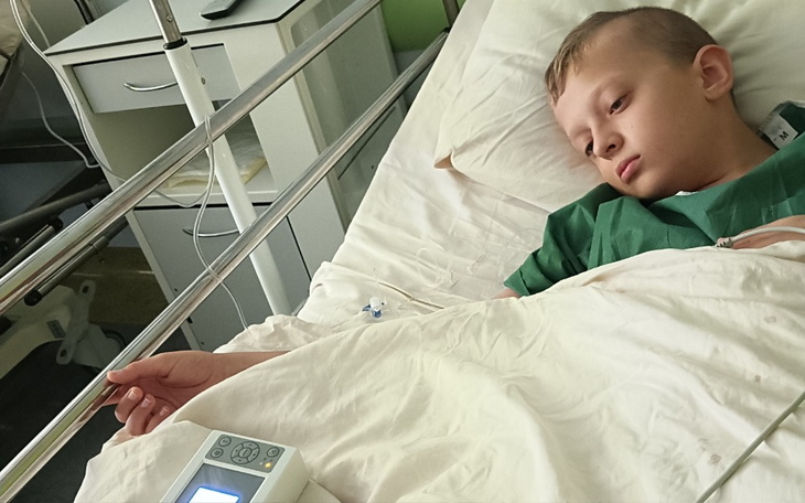 Chłopiec leżący w szpitalnym łóżku, wyglądający na zamyślonego.