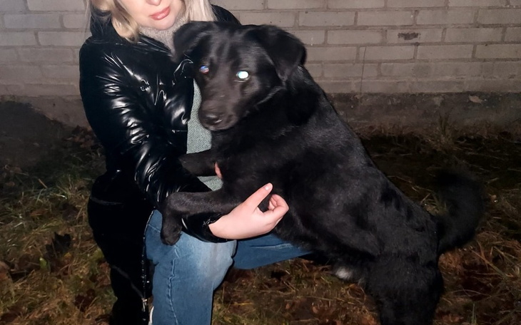 Kobieta trzyma czarnego psa w nocy, oboje uśmiechnięci.