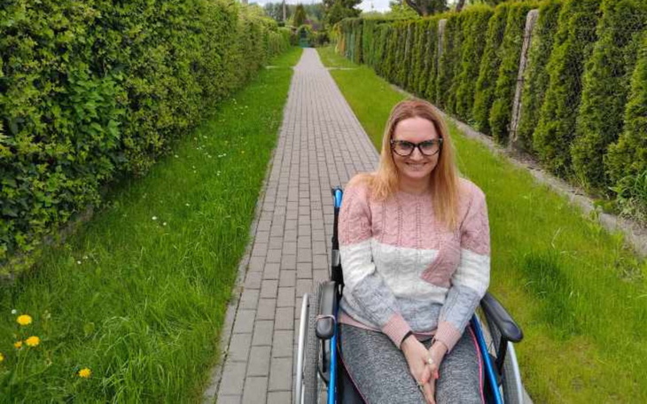 Kobieta na wózku inwalidzkim, uśmiechająca się na ścieżce.