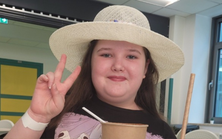 Dziewczynka w kapeluszu trzymająca napój i pokazująca znak pokoju.