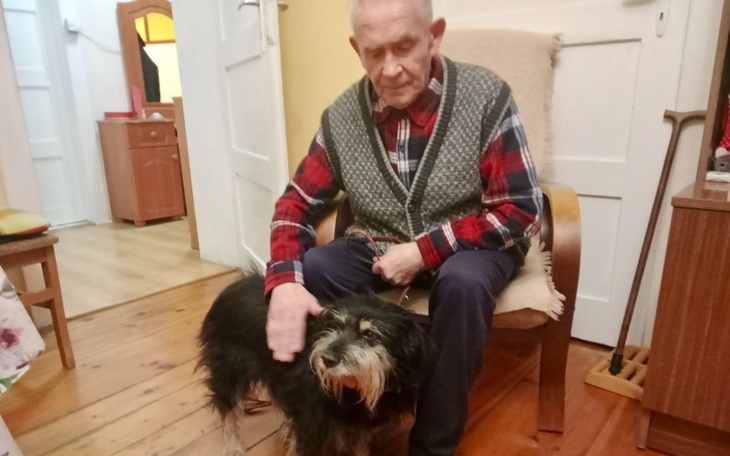 Starszy mężczyzna głaszcze psa w przytulnym wnętrzu.