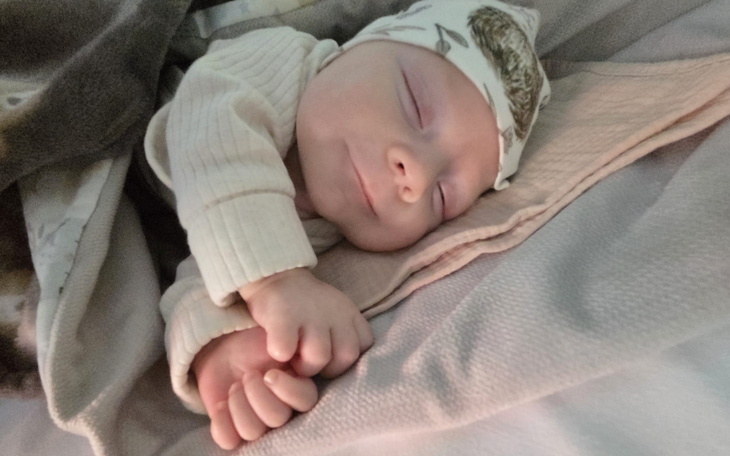 Śpiące niemowlę w czapeczce, z rączkami złożonymi na piersi.