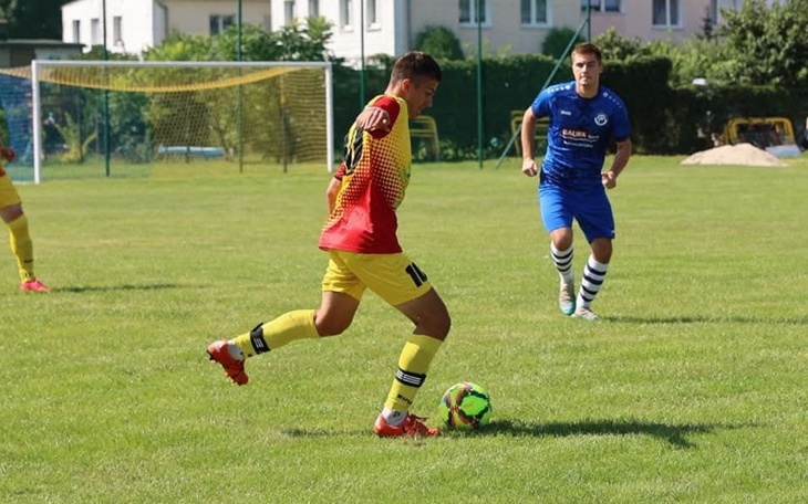 Młody piłkarz w akcji, strzela piłkę na boisku.