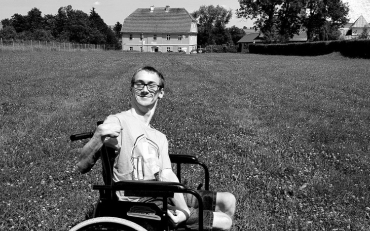 Mężczyzna na wózku inwalidzkim w zielonym otoczeniu.