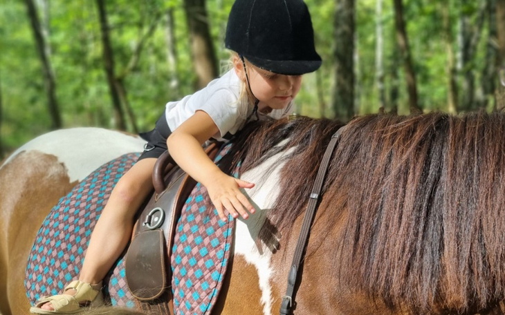 Dziewczynka jeździ na koniu w lesie, dotykając jego grzywy.