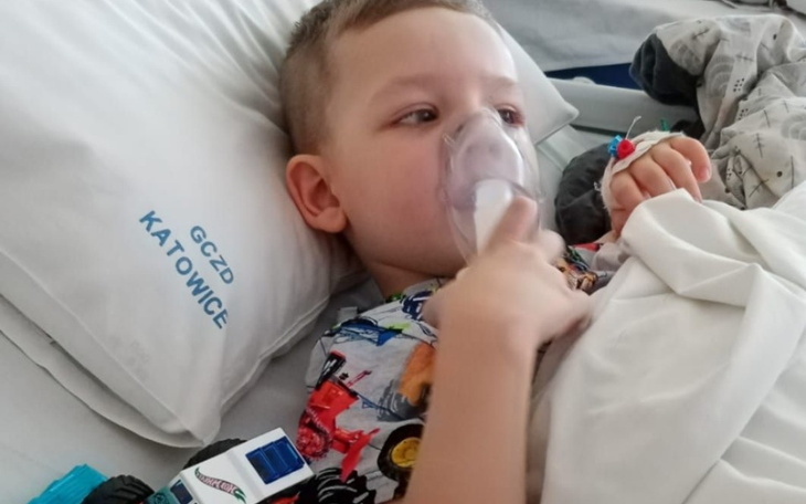Chłopiec w łóżku z maską tlenową, trzymający zabawkę w ręku.