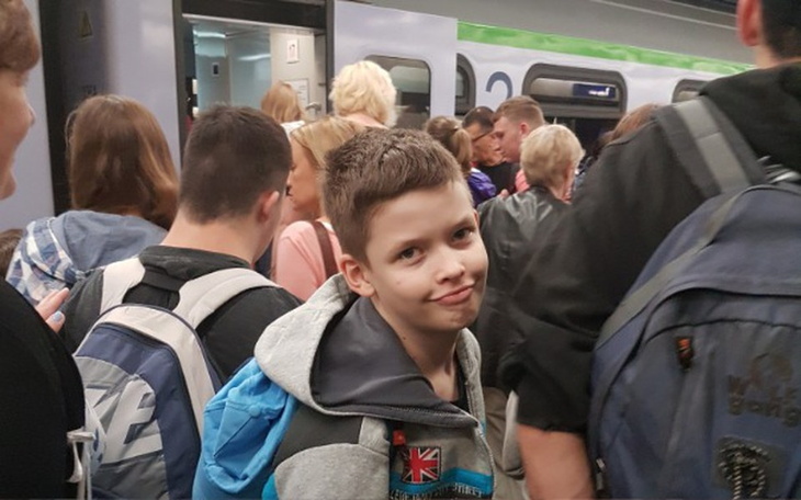 Chłopiec w tłumie na stacji kolejowej, z uśmiechem na twarzy.