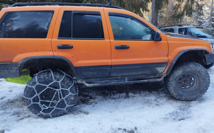 Pomarańczowy SUV z łańcuchami na oponach na zaśnieżonej drodze.
