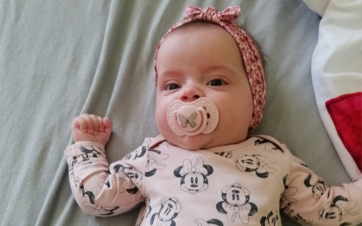 Małe dziecko w śpioszkach z Miki, z smoczkiem w buzi.