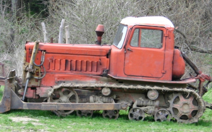 Stary ciągnik na polu, pokryty rdzą i zarośnięty trawą.