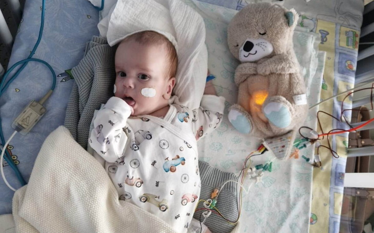 Małe dziecko w szpitalu, trzymające pluszowego misia, z monitorami wokół.