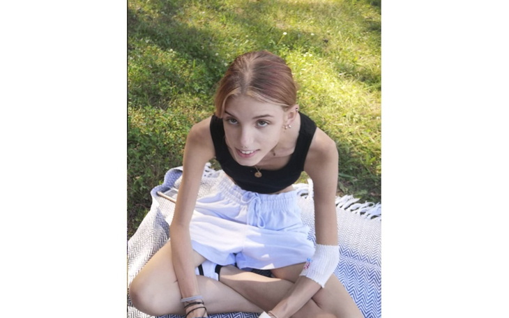 Młoda dziewczyna siedząca na kocu w parku, uśmiechająca się do kamery.